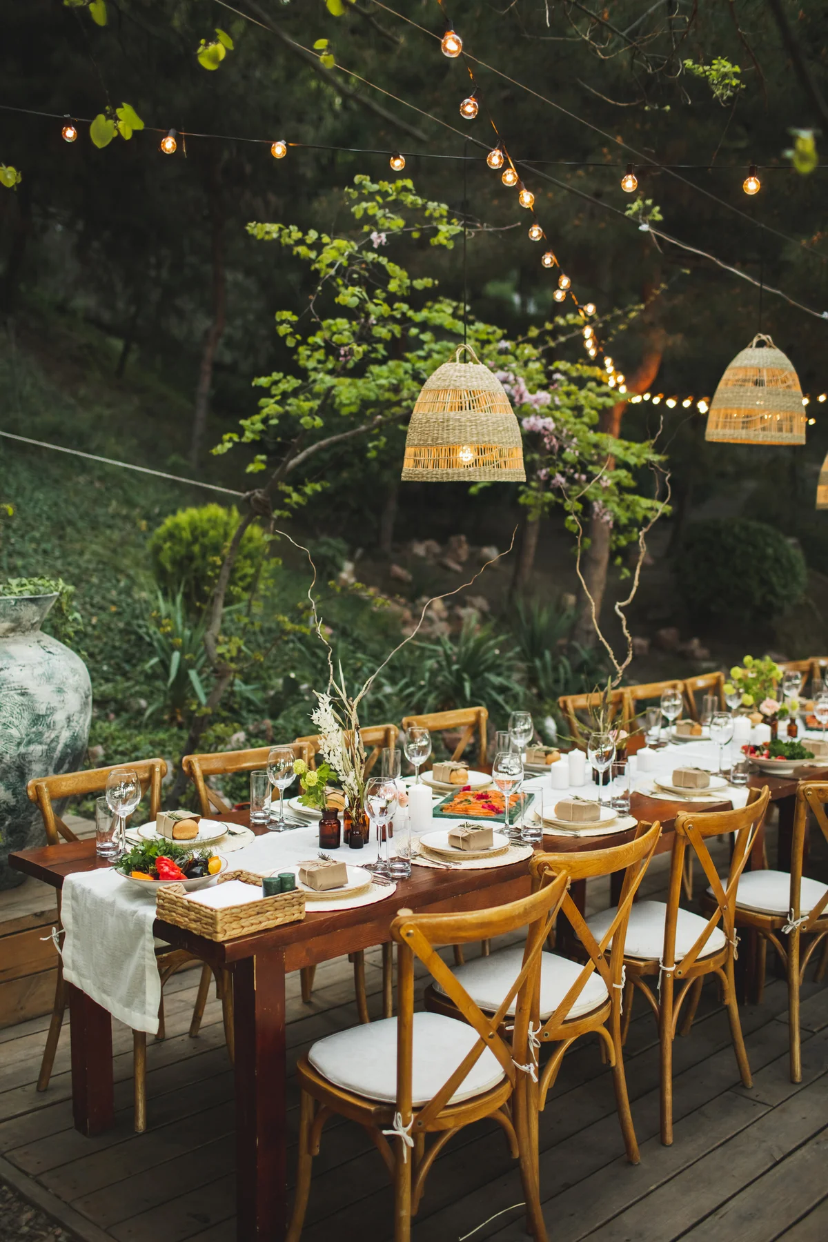 Trendy and beautiful table setting for romantic wedding dinner in rust boho style, with lights and lanterns above.