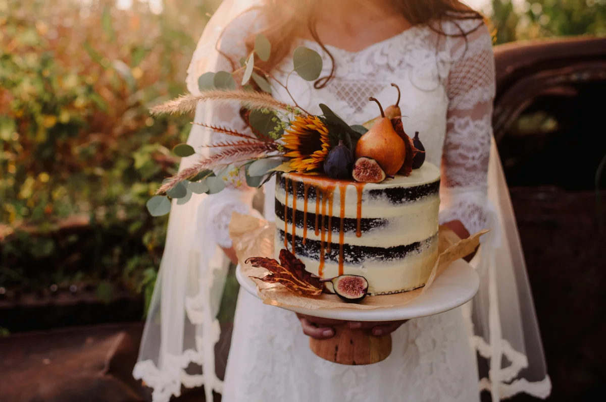 Bride holding boho wedding cake at sunset