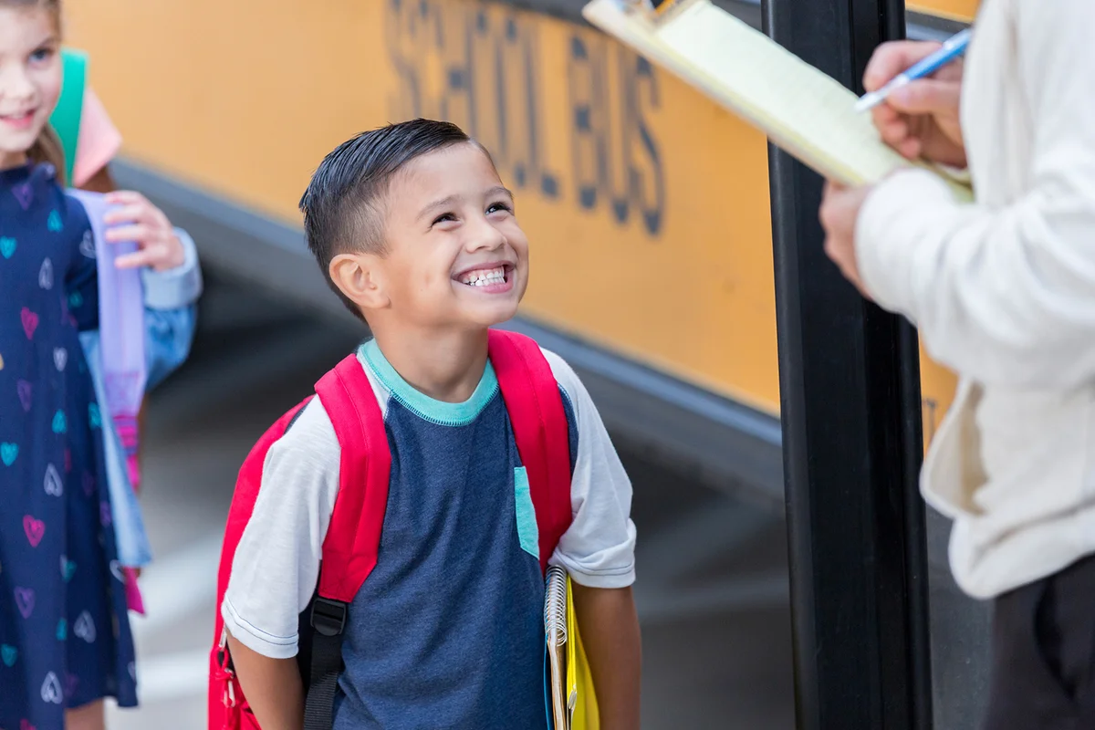 Excited elementary school boy greets bus driver as he prepares to load the bus