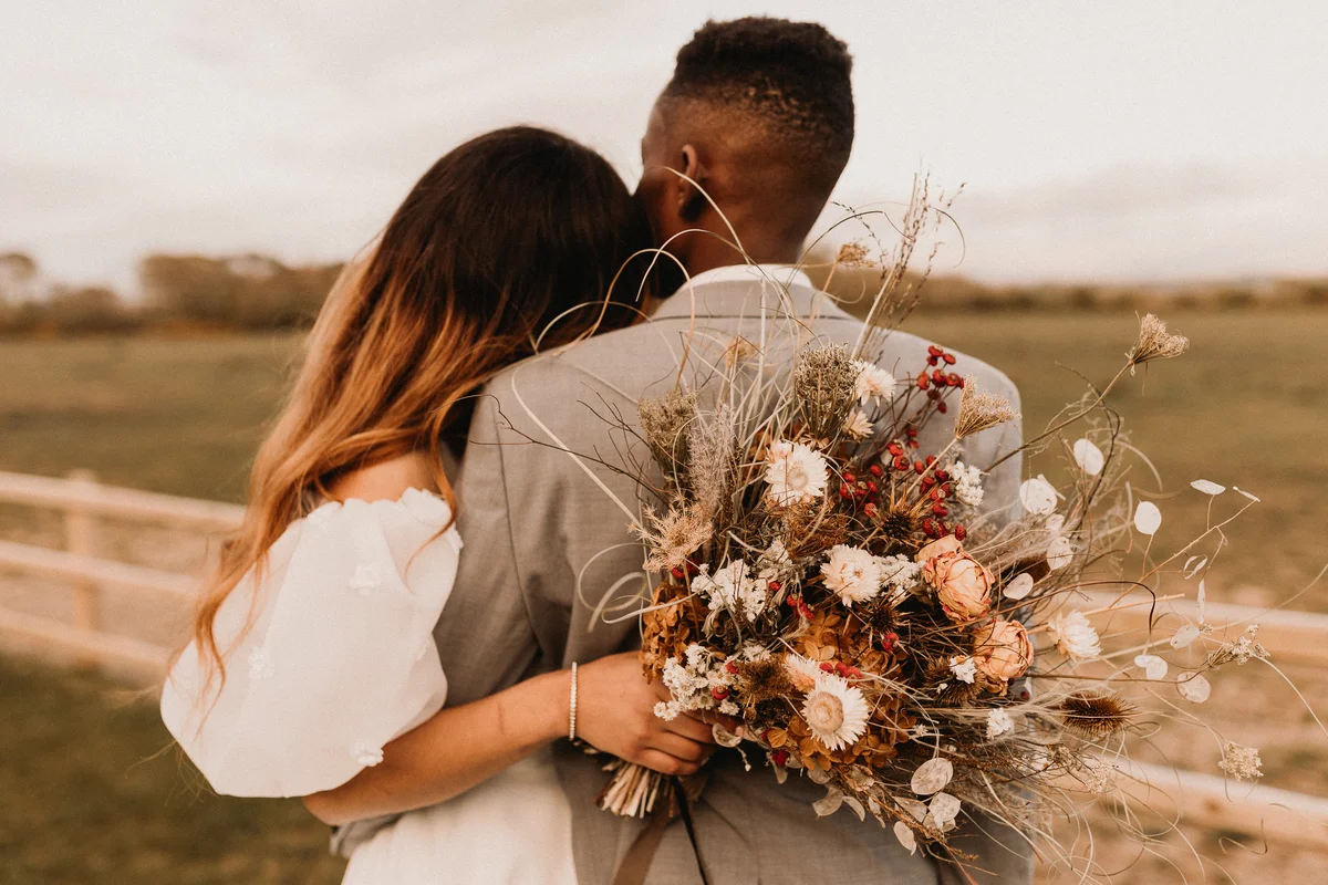 Young couple posing for wedding photos with boho bouquet of flowers