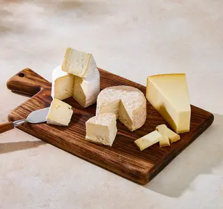Wooden board with three gourmet cheeses. 