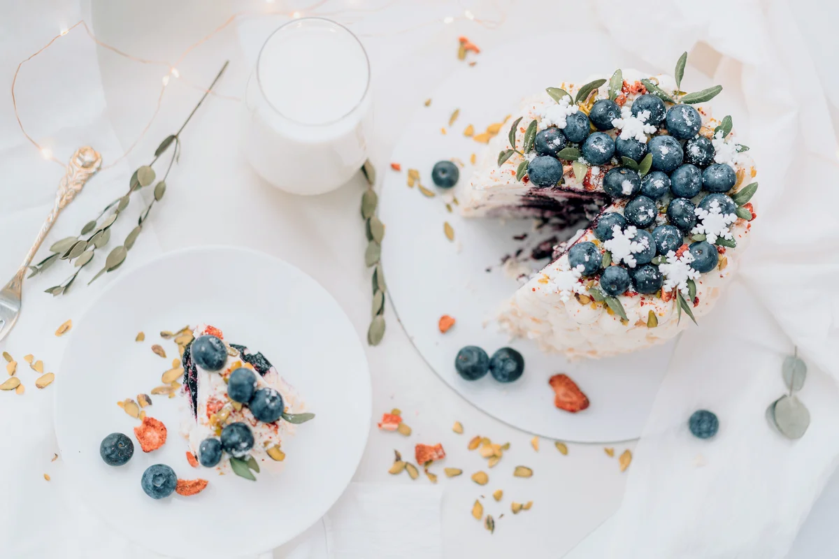 Sliced meringue cake with blueberries and glass of milk on white table