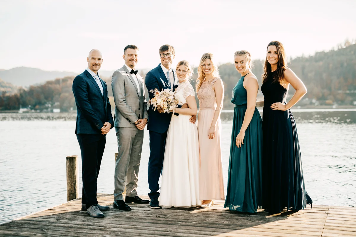 Bride and groom standing along with friends on jetty over lake