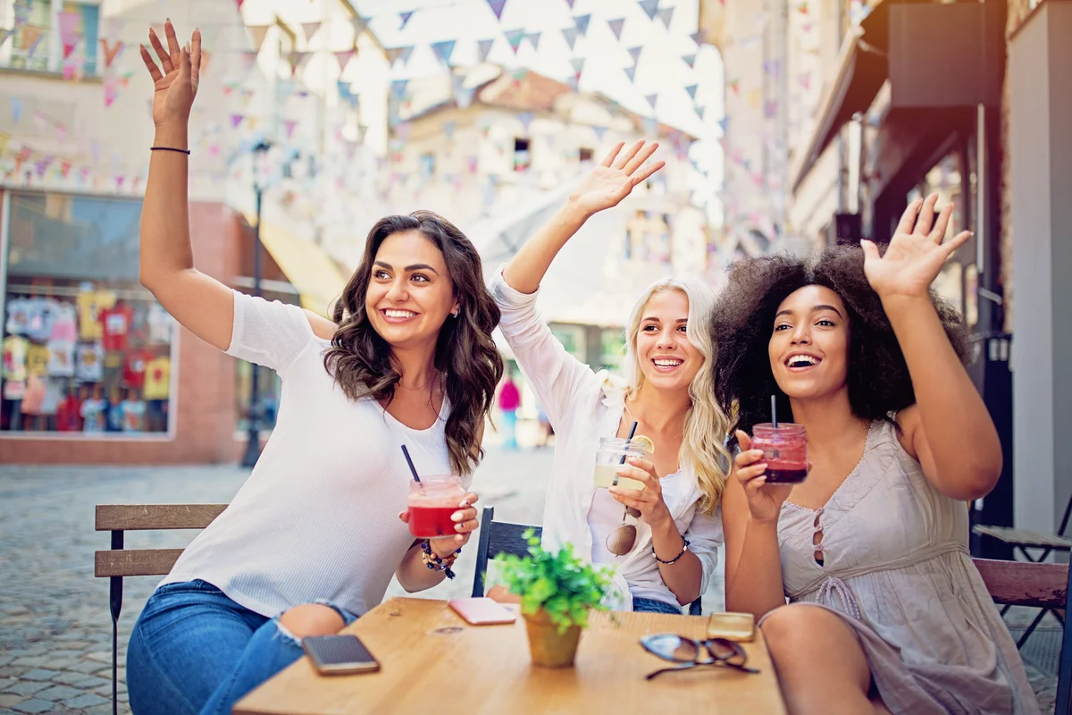 Girlfriends drinking cocktails and waiving their friends in the cafe