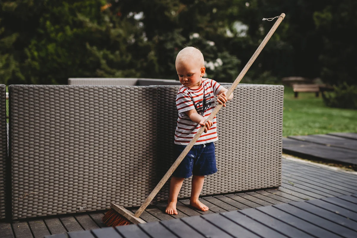 child barefoot sweeping backyard patio with big broom