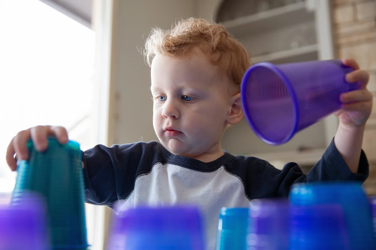 Cute boy playing, stacking blue cups in living room at home
