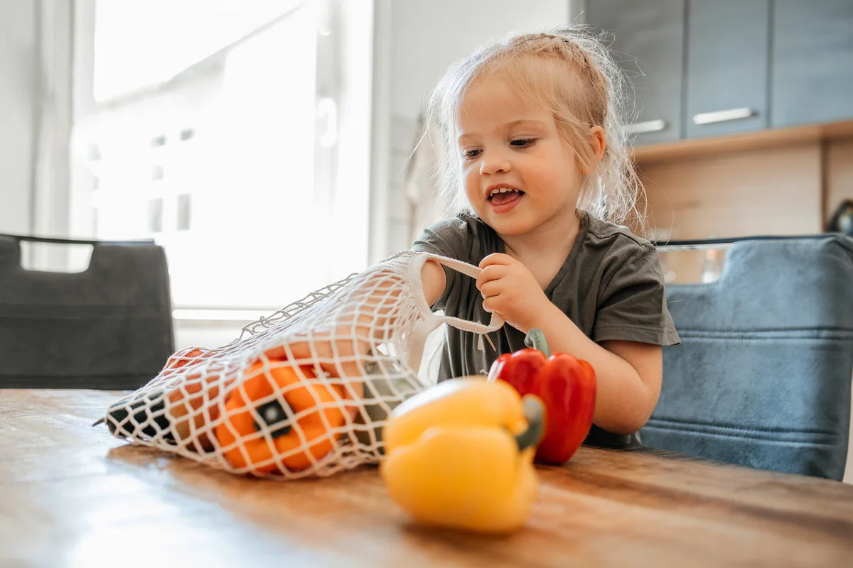 girl sits on a chair in the kitchen and sorts fresh vegetables bought at the market