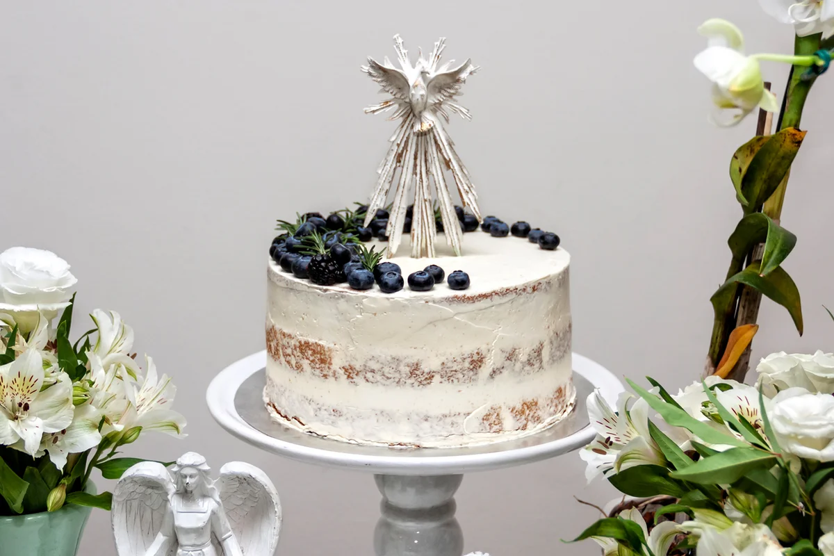 White naked cake with berries on top with many white flowers around