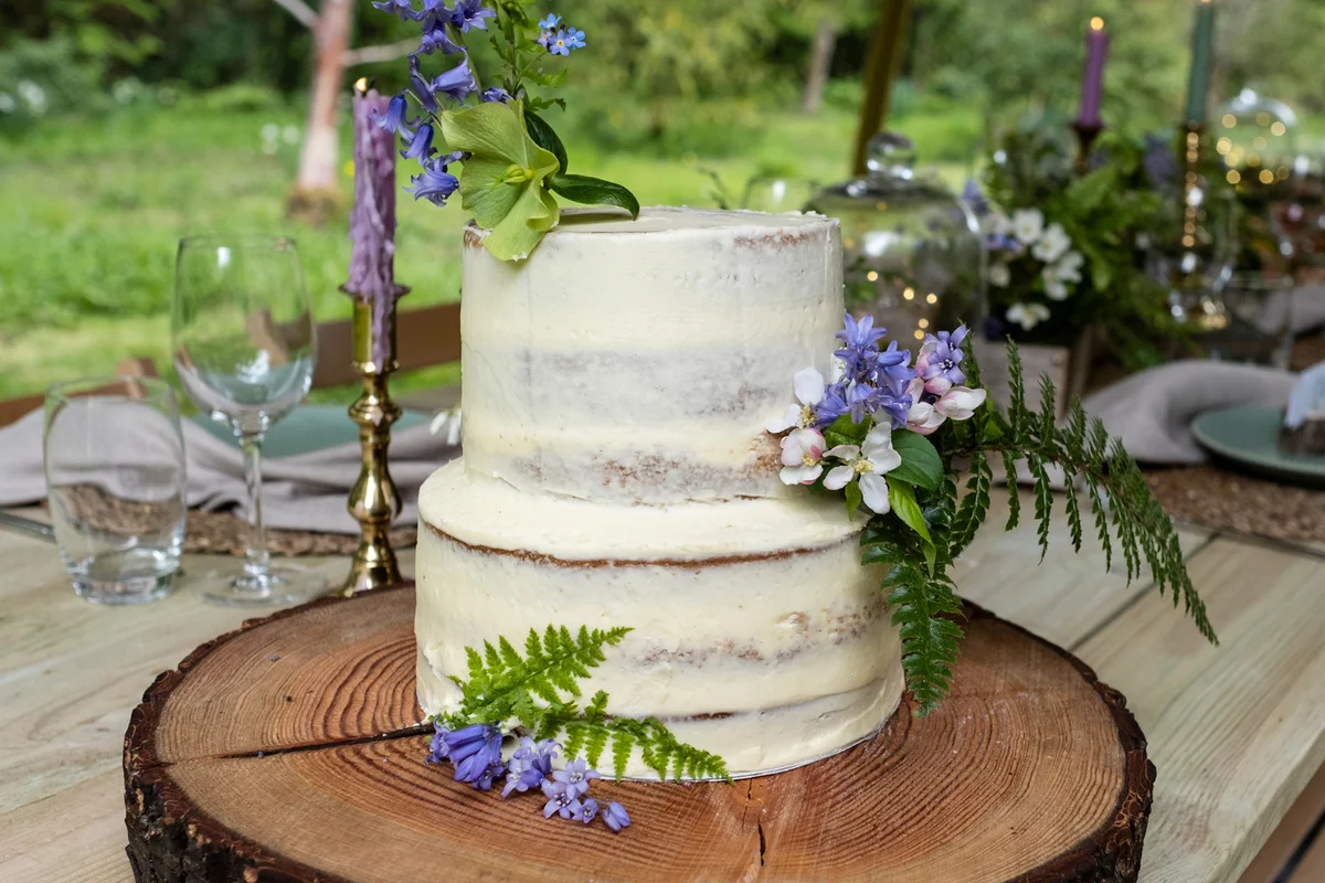 Close up of two tiered cake with flower decorations on a tree slice for a naming ceremony in a forest