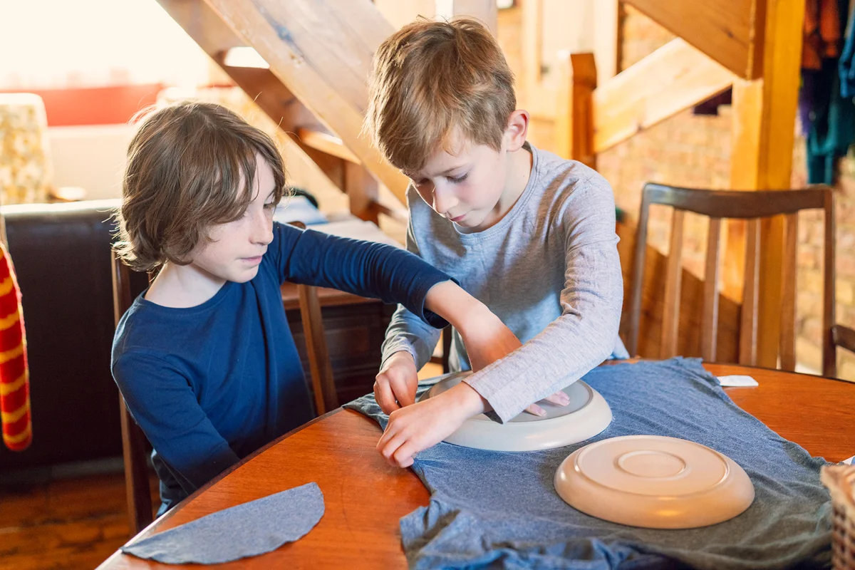 Two young brothers drawing around a plate to get the shape to make a face mask from an old t shirt.