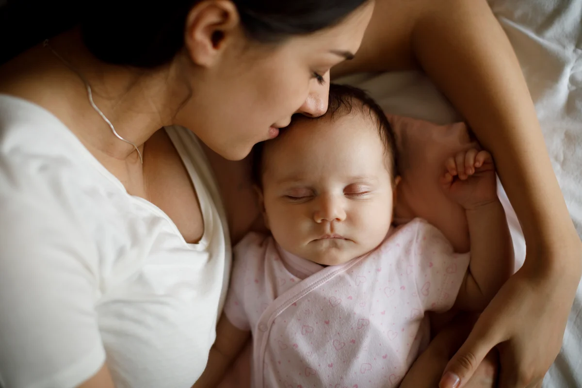 Young mother and her baby girl sleeping in bed at home