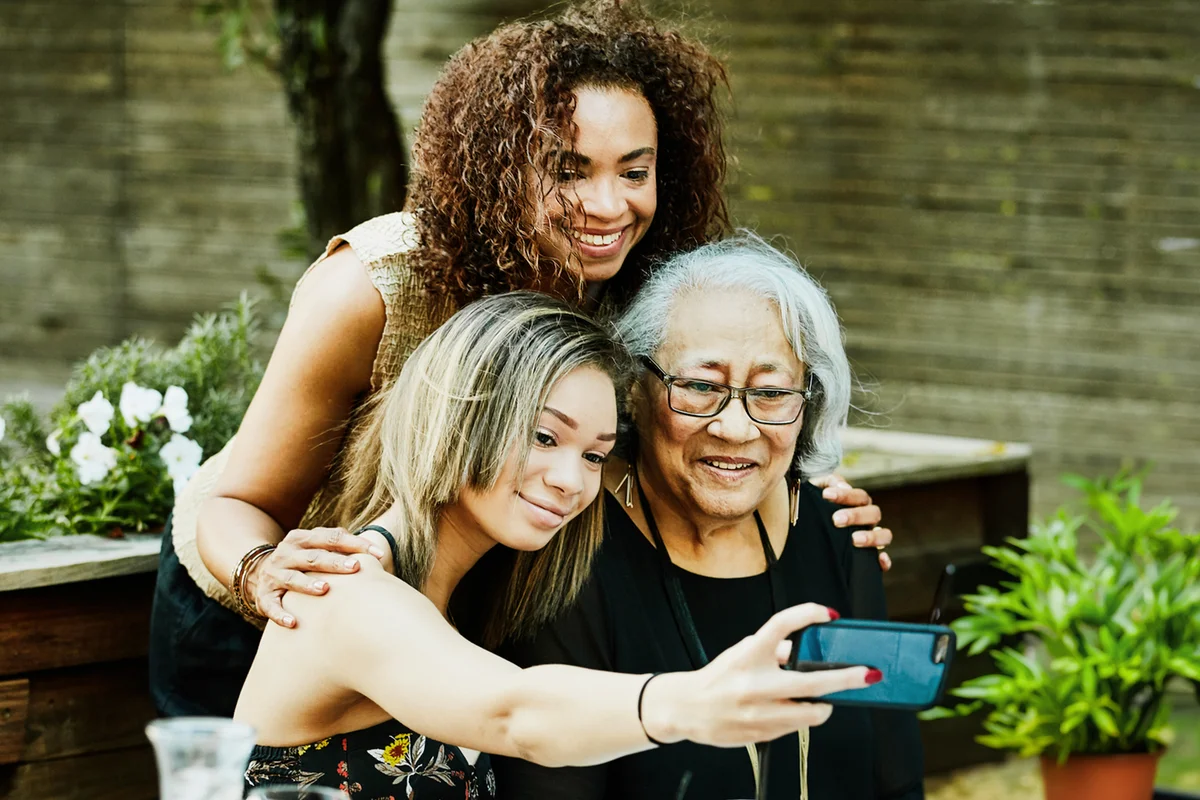 Teenage girl taking selfie with smartphone of mother and grandmother during outdoor family dinner party