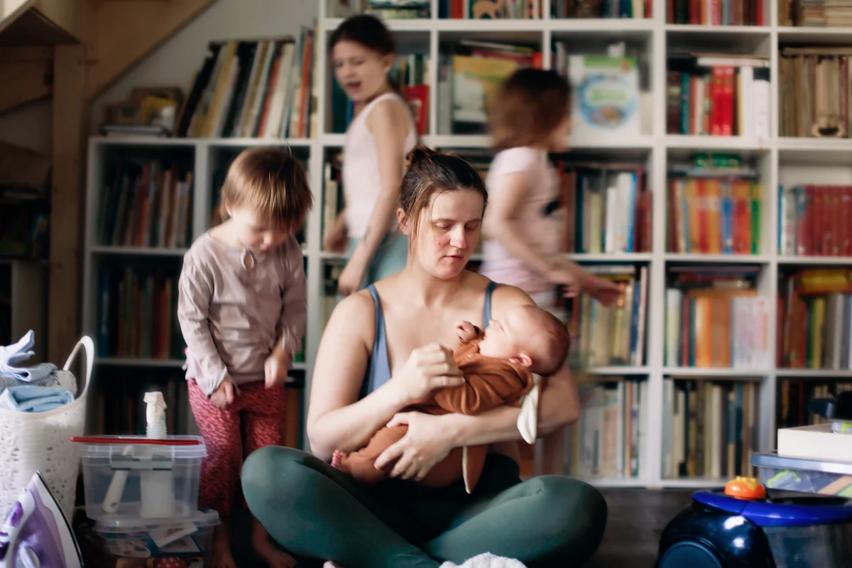 Burnt-out mother with baby in her arms and children running around