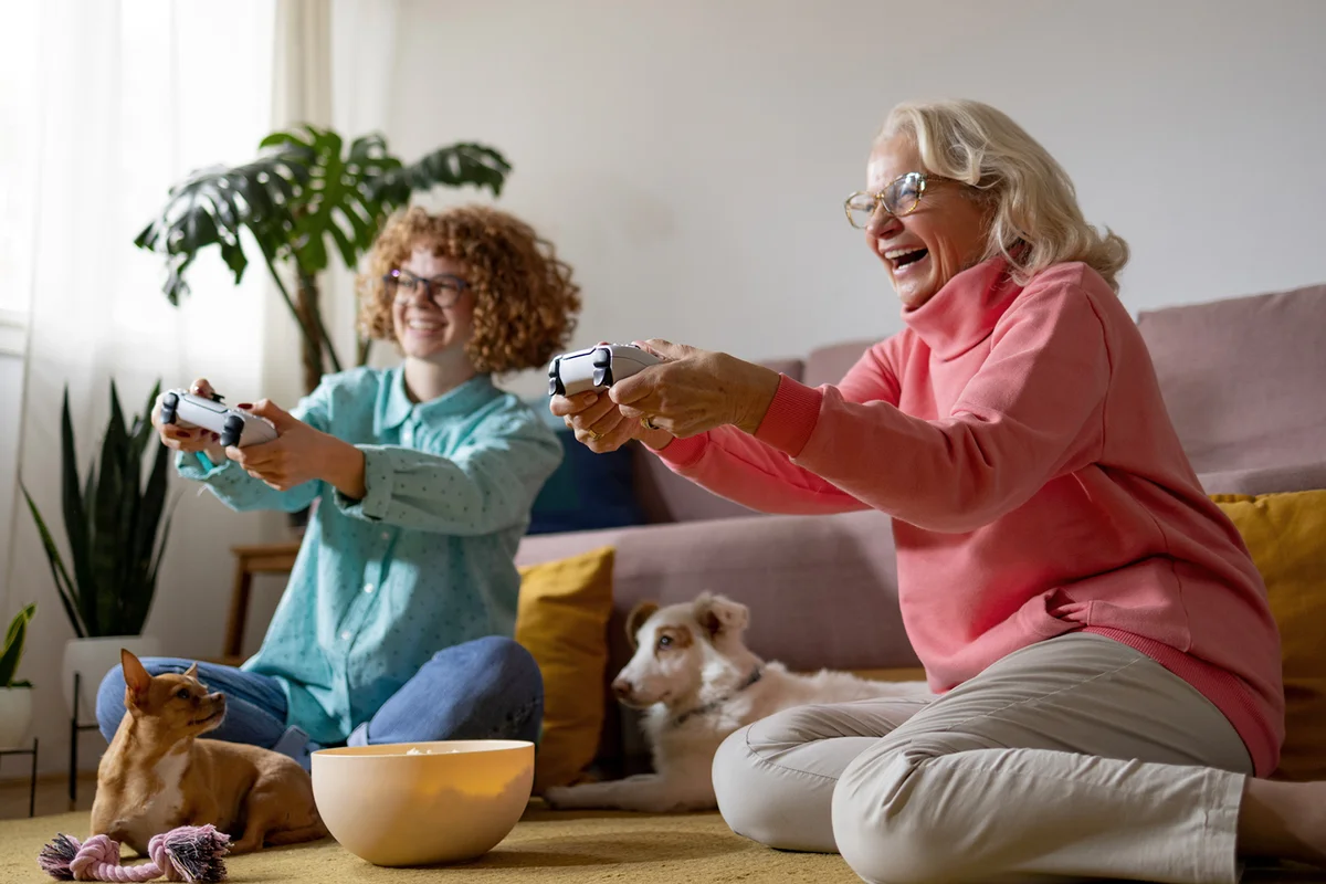 girl playing playstation with her grandmother at home with their pets enjoying time together