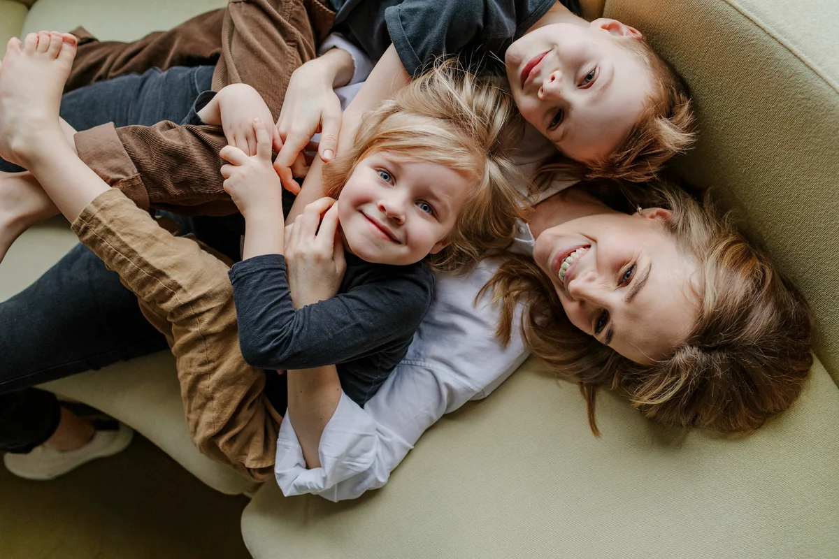 Mother lying with sons on sofa in living room at home
