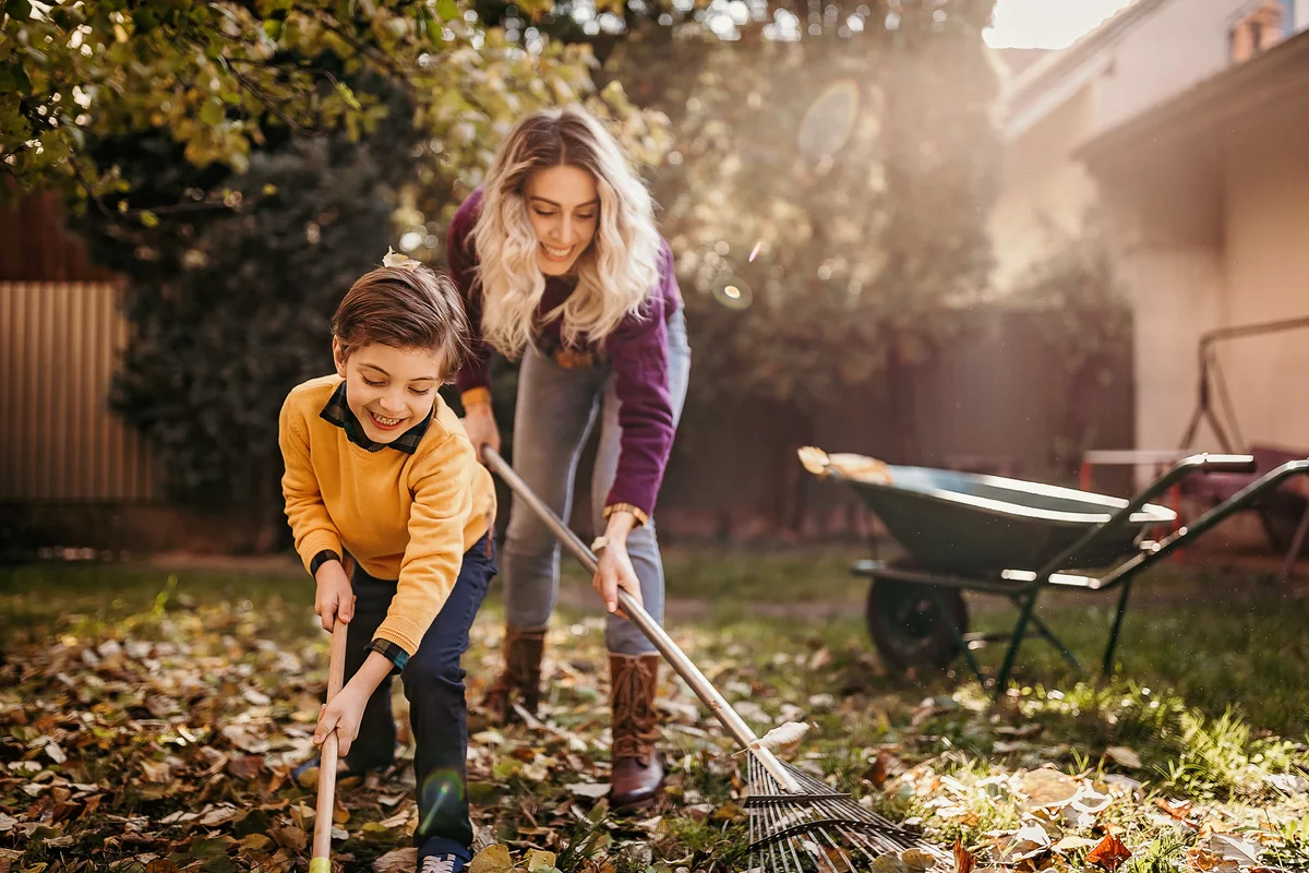 Mother and son playing in backyard cleaning autumn leaves