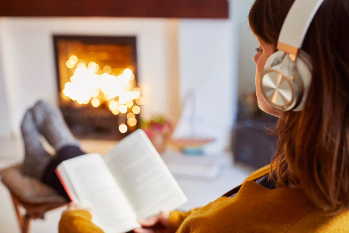 Woman with headphones reading in living room with fireplace