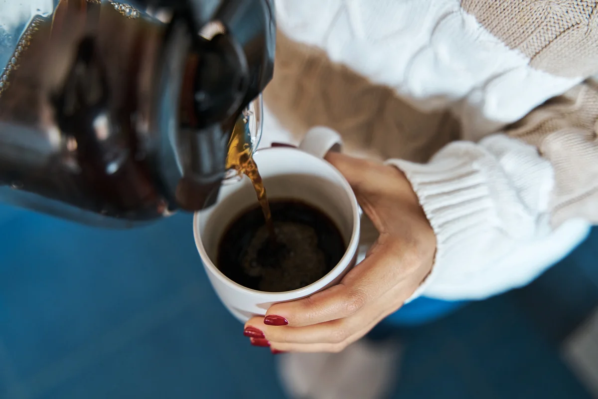 Woman pouring hot coffee to a mug at home