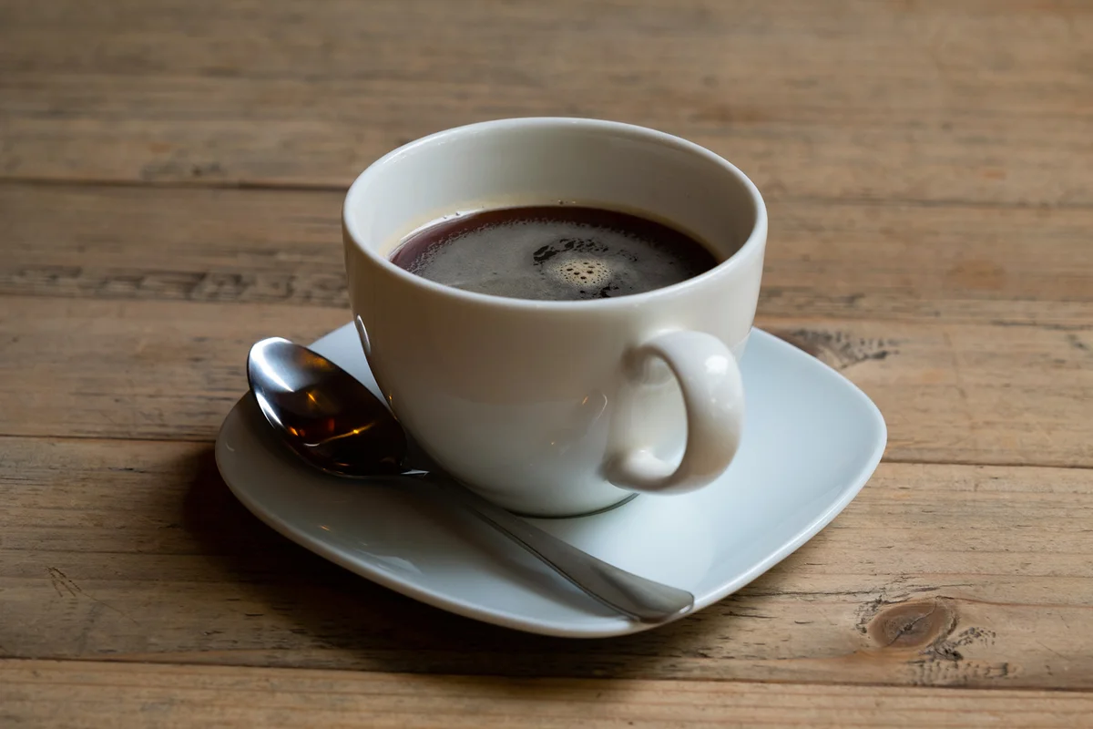 One glass of black tea, chicory or coffee on a light wood table