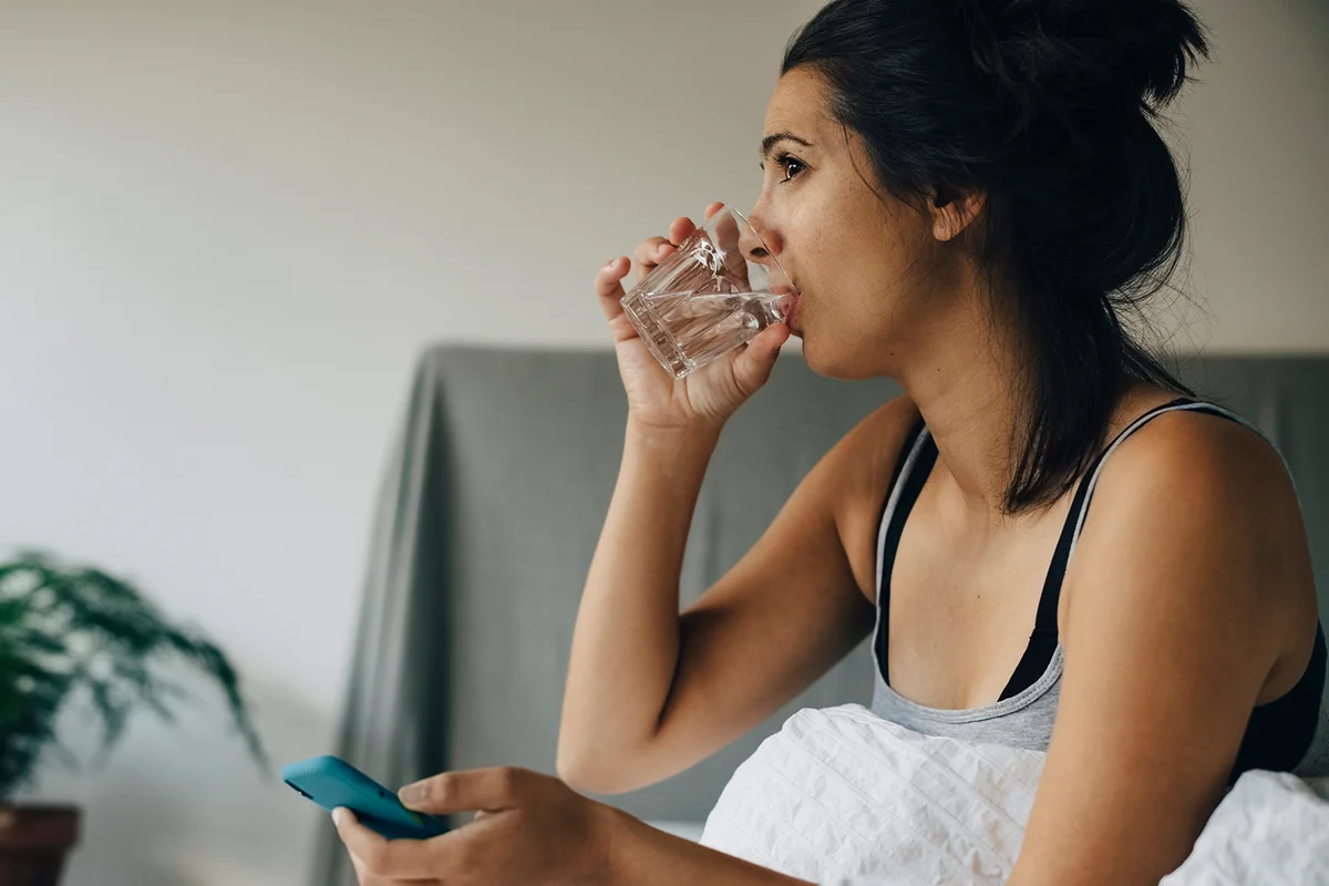 Woman taking water while sitting on bed at home