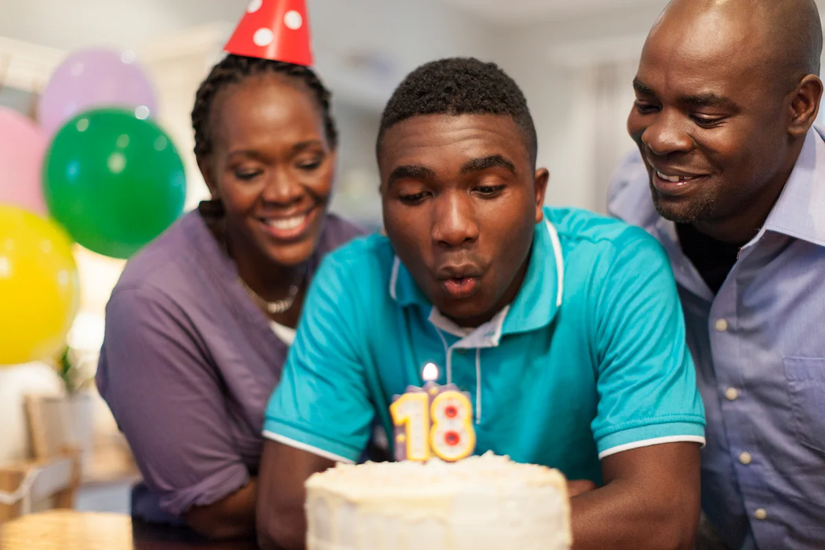 teenager blowing out the candles on his 18th birthday cake surrounded by his family