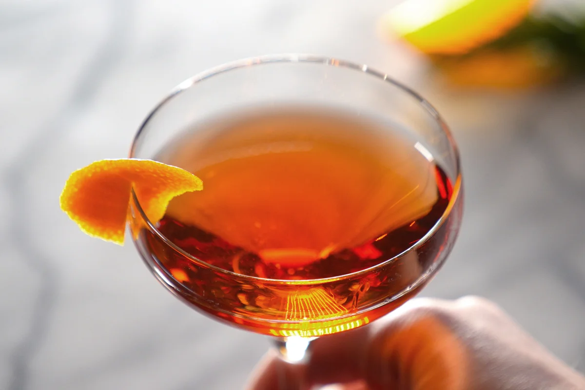 A hand holds the stem of a refreshing cocktail with distinctive orange coloring and garnish
