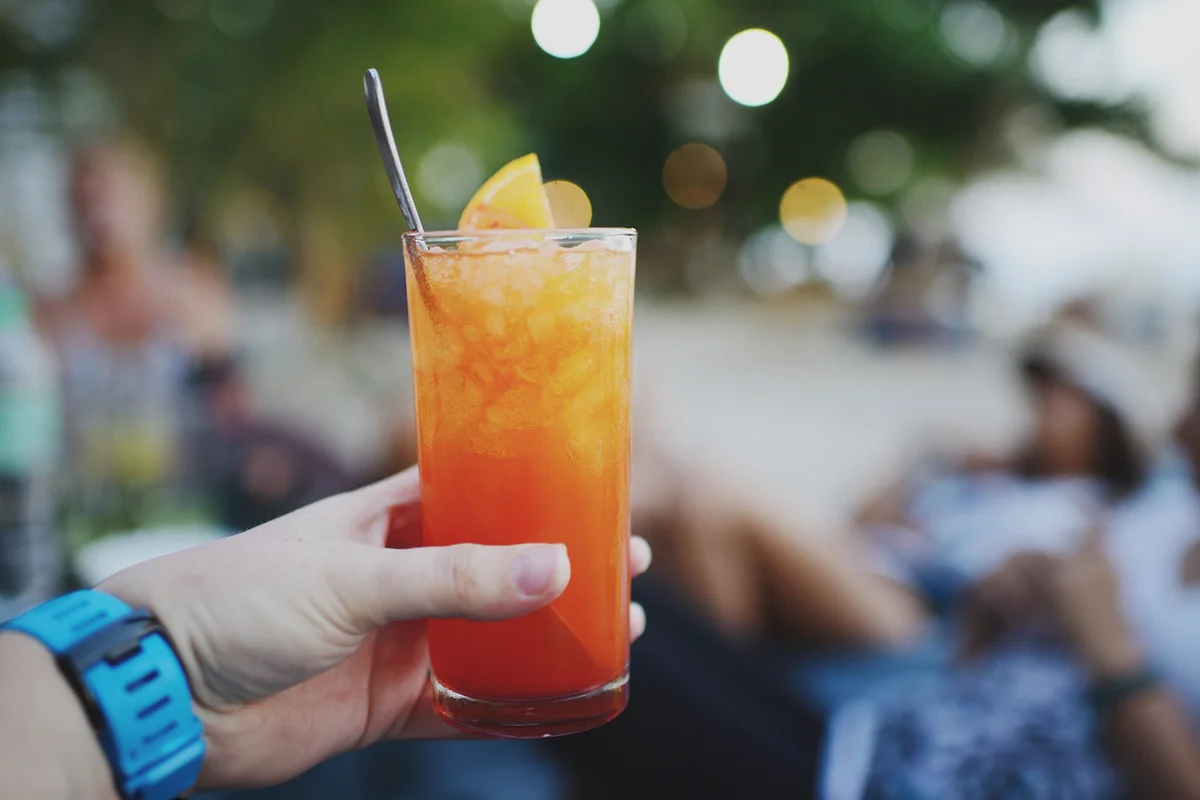 Hand holding bright red and orange frozen cocktail on the beach