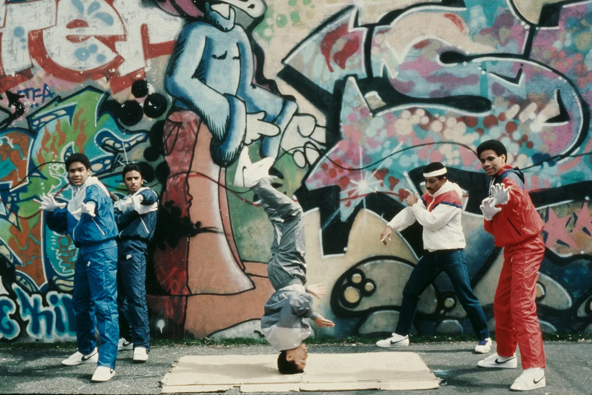 Teenagers breakdancing next to a wall covered in grafitti