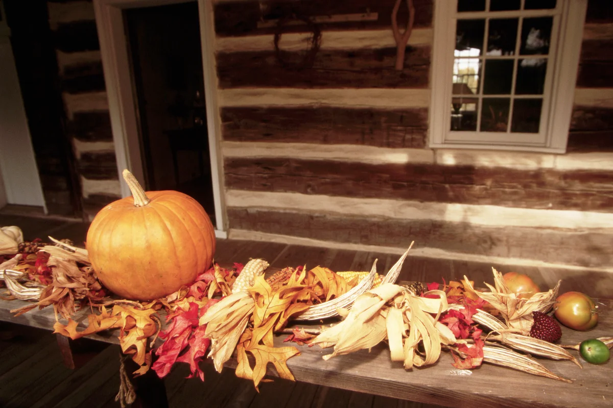 Leaves, vegetables, and a pumpkin line a porch rail