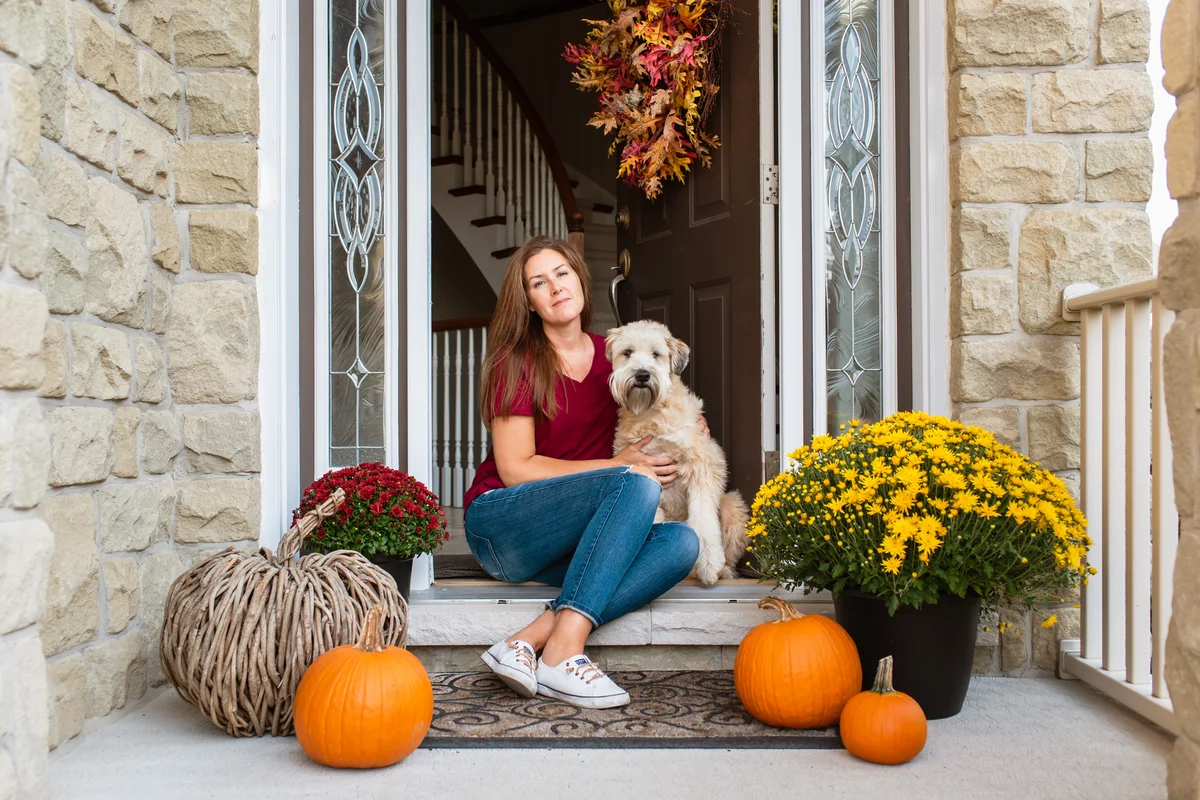Woman and her dog sitting in doorway of home decorated for fall