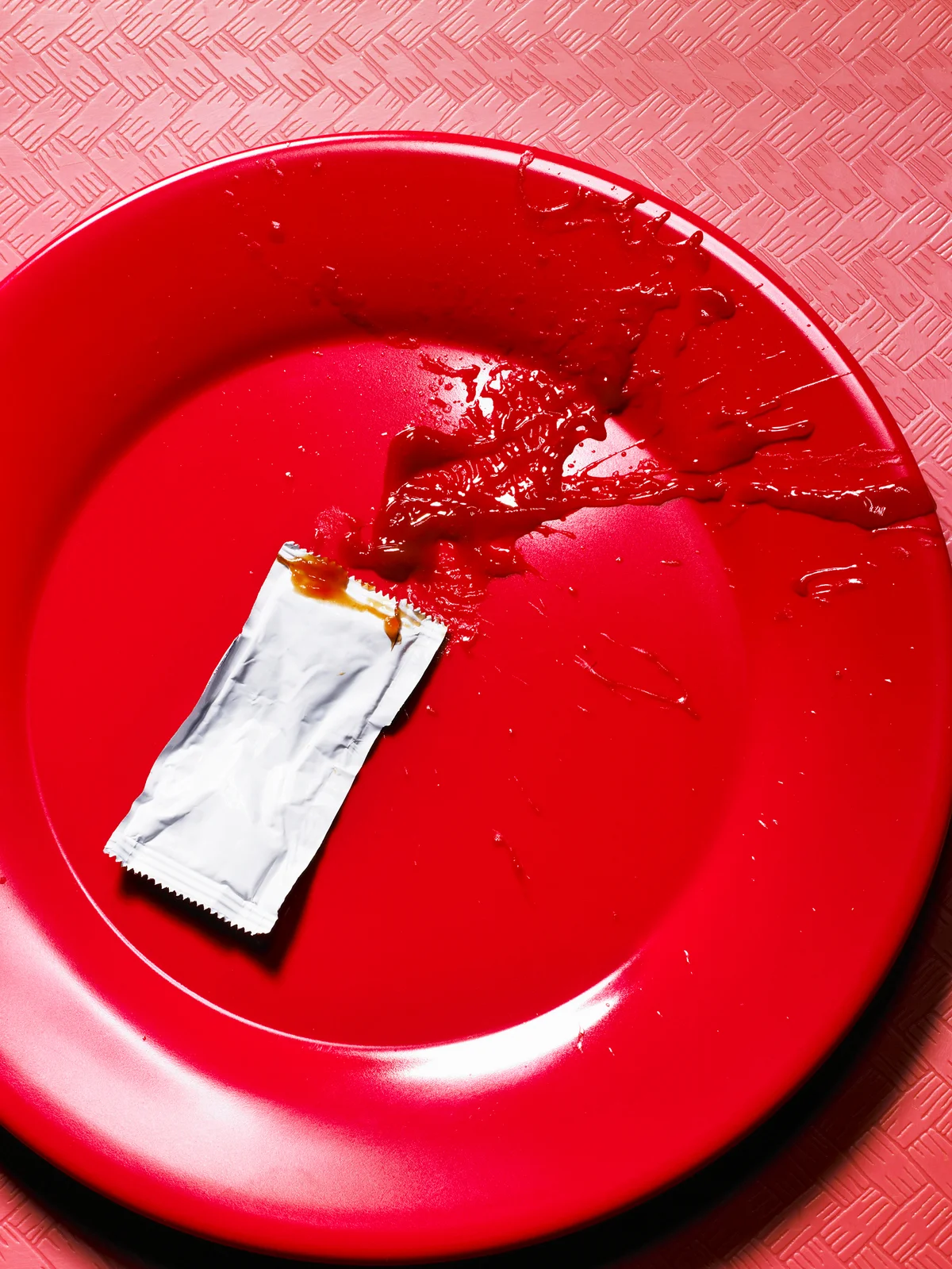 Splattered ketchup packet onto red plate
