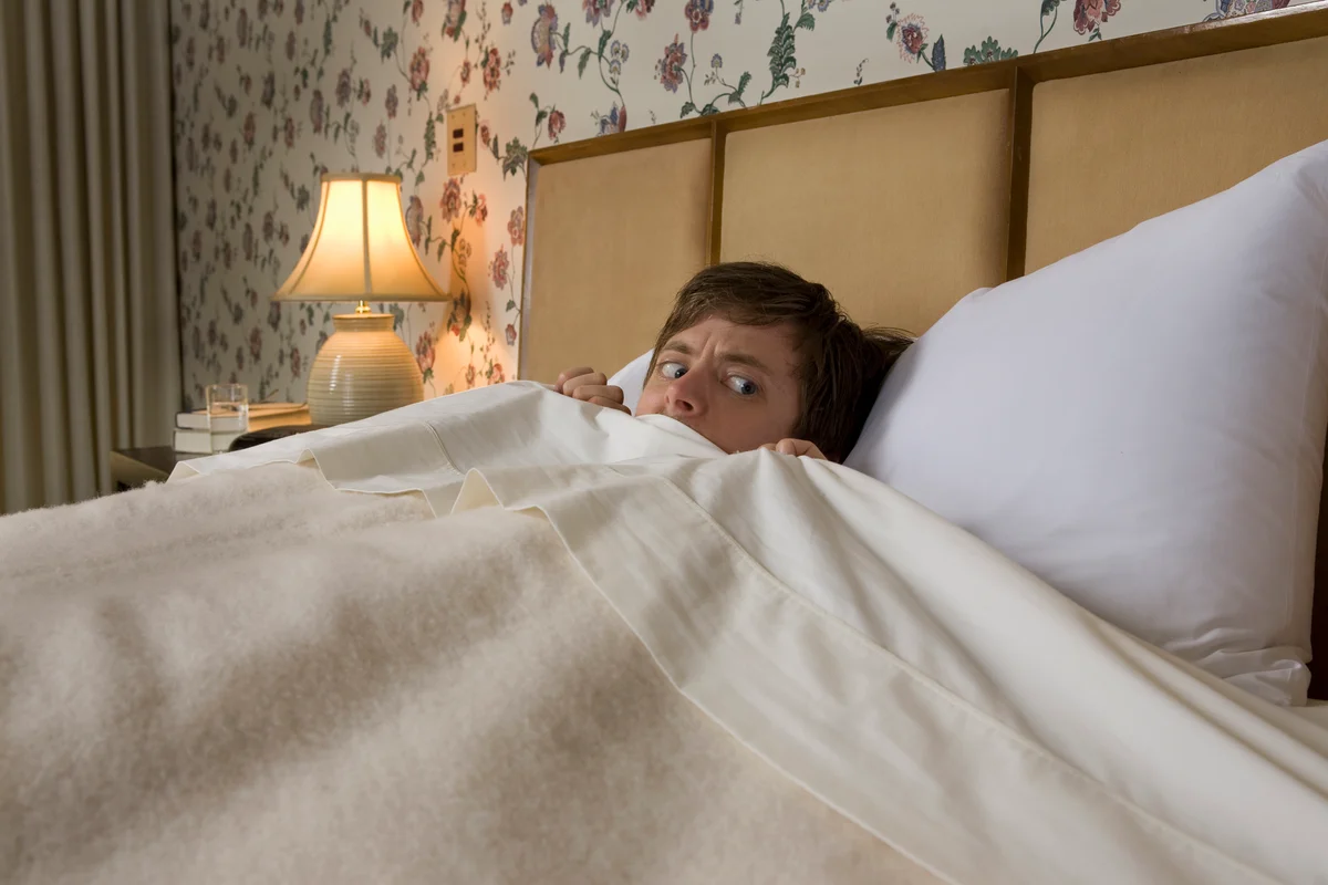 A scared man in bed pulling covers up to his chin