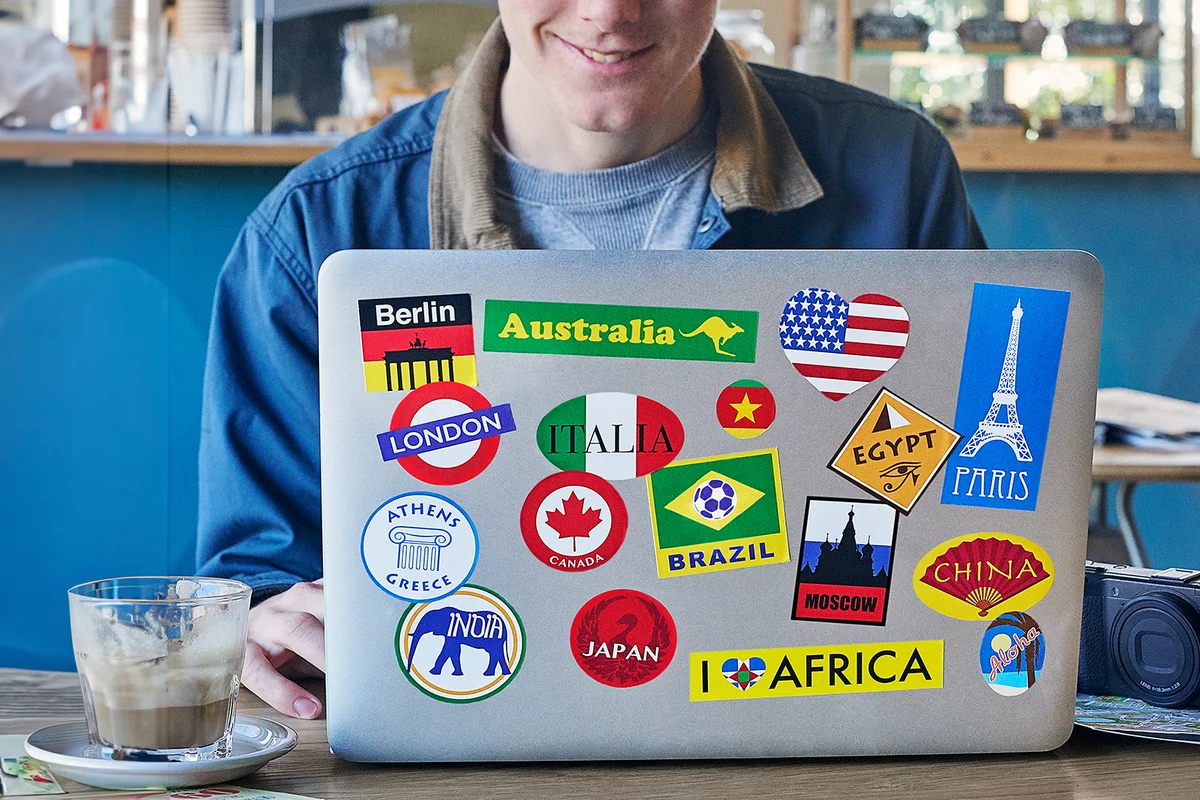 Young man using a laptop with travel stickers