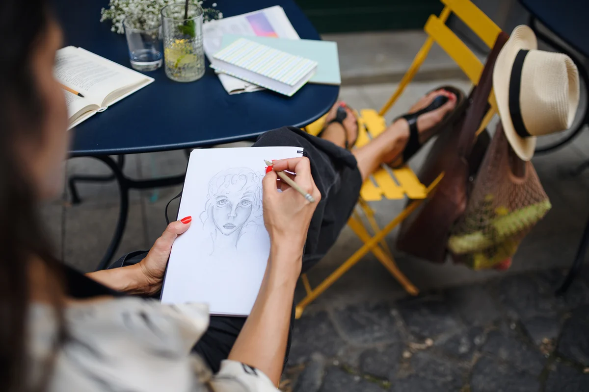 Unrecognizable woman artist drawing pictures outdoors in café