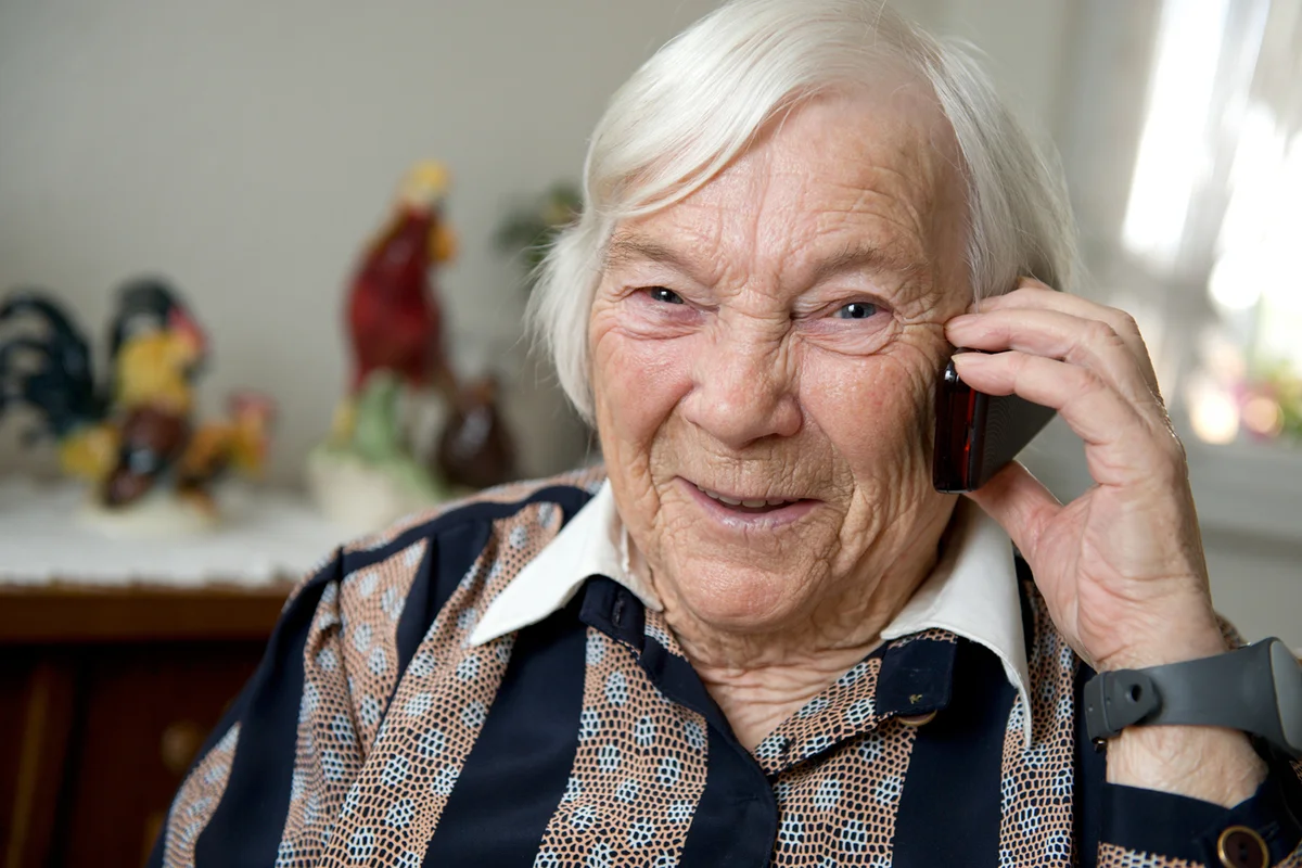 Female senior smiles into the camera and the phone with her family