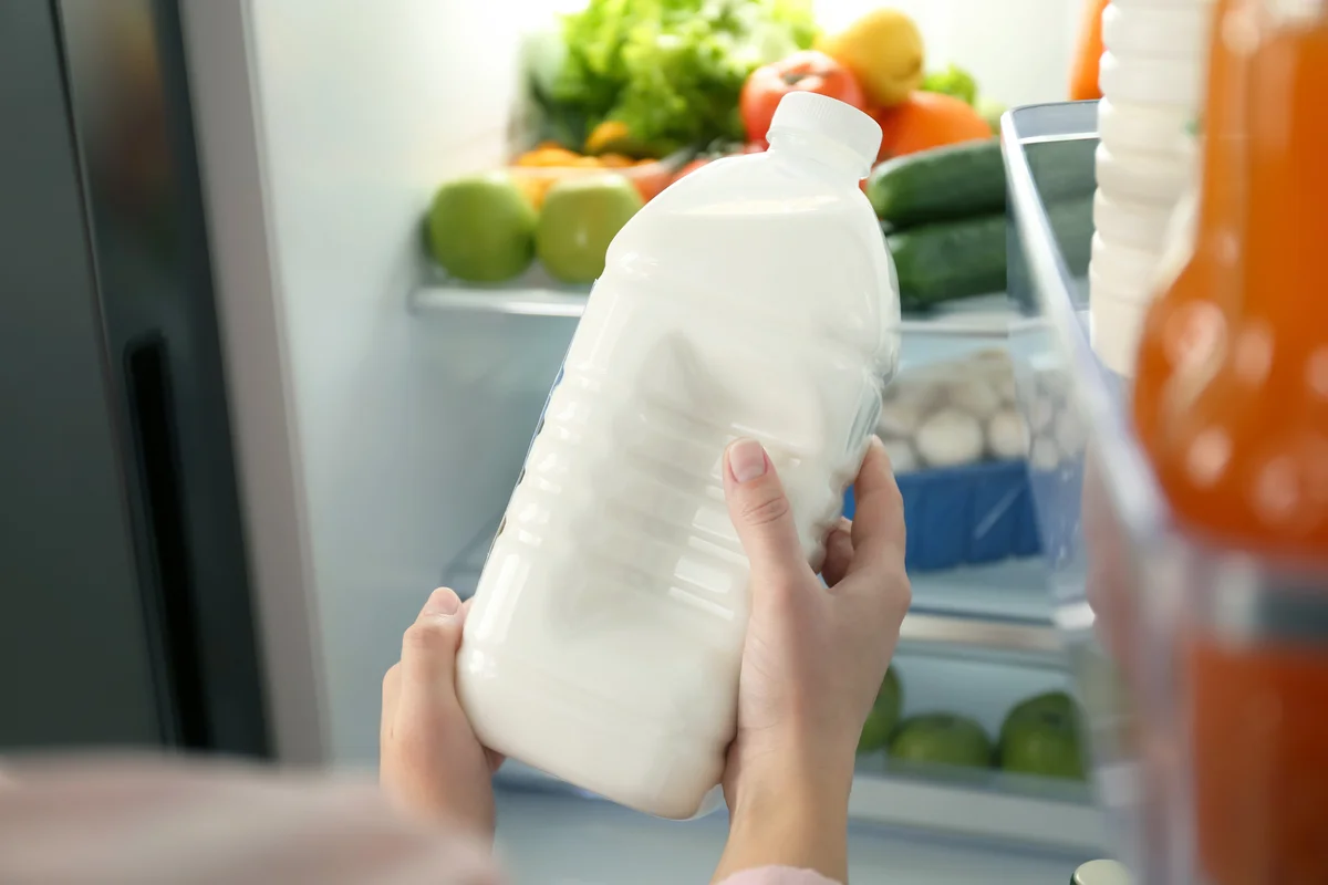 Woman with gallon of milk near refrigerator