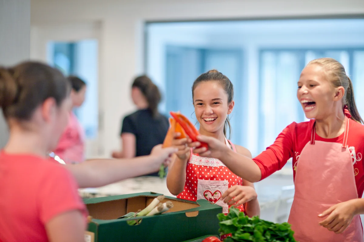 Teenage girls holding up chillies and carrot in kitchen