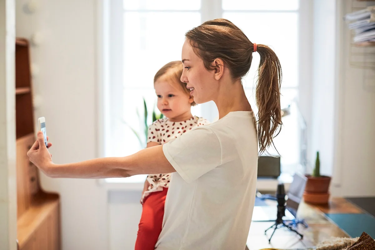 Female influencer taking selfie with daughter through smart phone at home