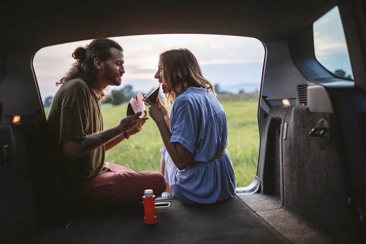 Couple eating watermelon in the back of their car to avoid bugs