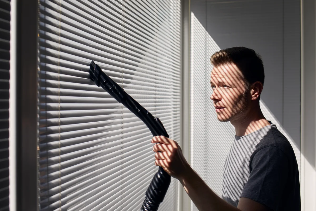 Man vacuuming window blinds