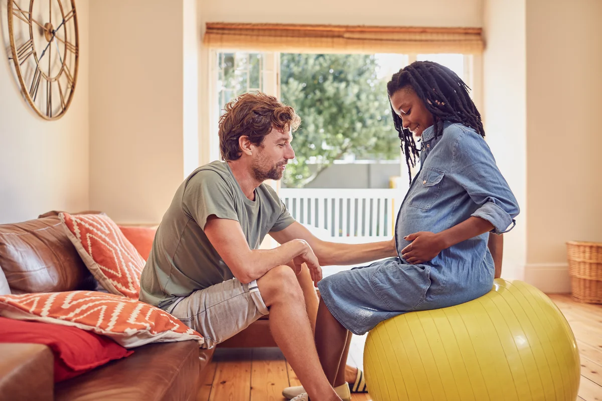 Pregnant woman sitting on exercise ball while husband supports her