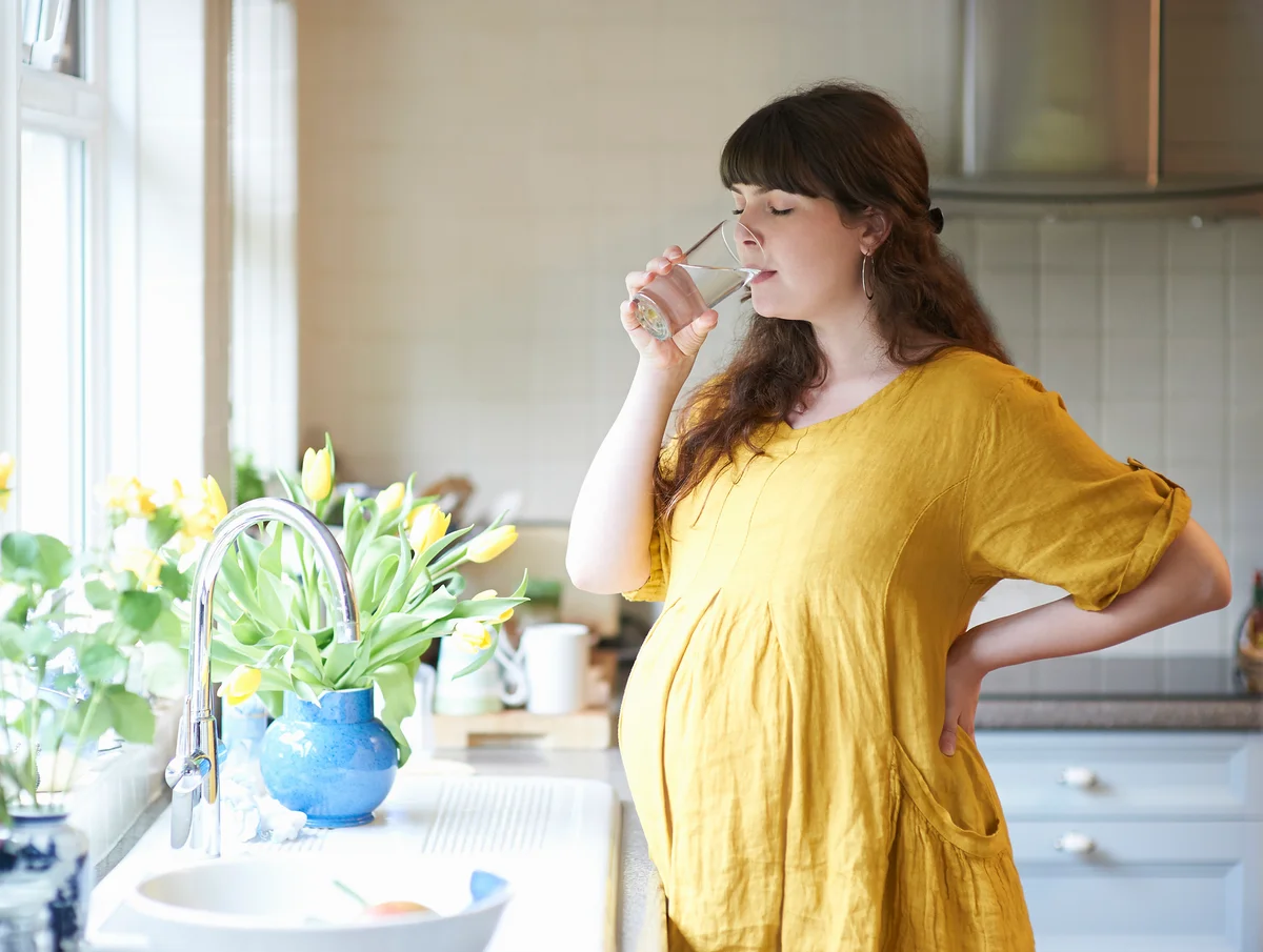 Pregnant woman drinking glass of water in kitchen