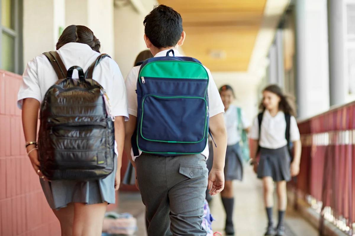 Two kids walking, one with leather backpack