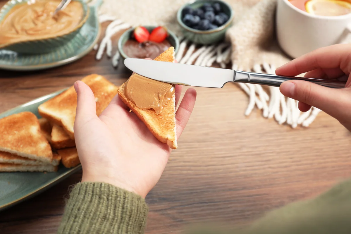 Woman spreading peanut butter onto toast at wooden table