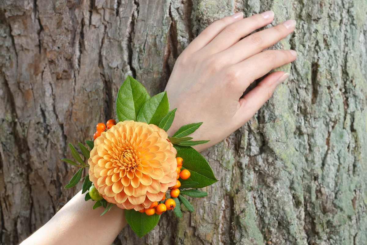 Orange and green wrist corsage on a hand