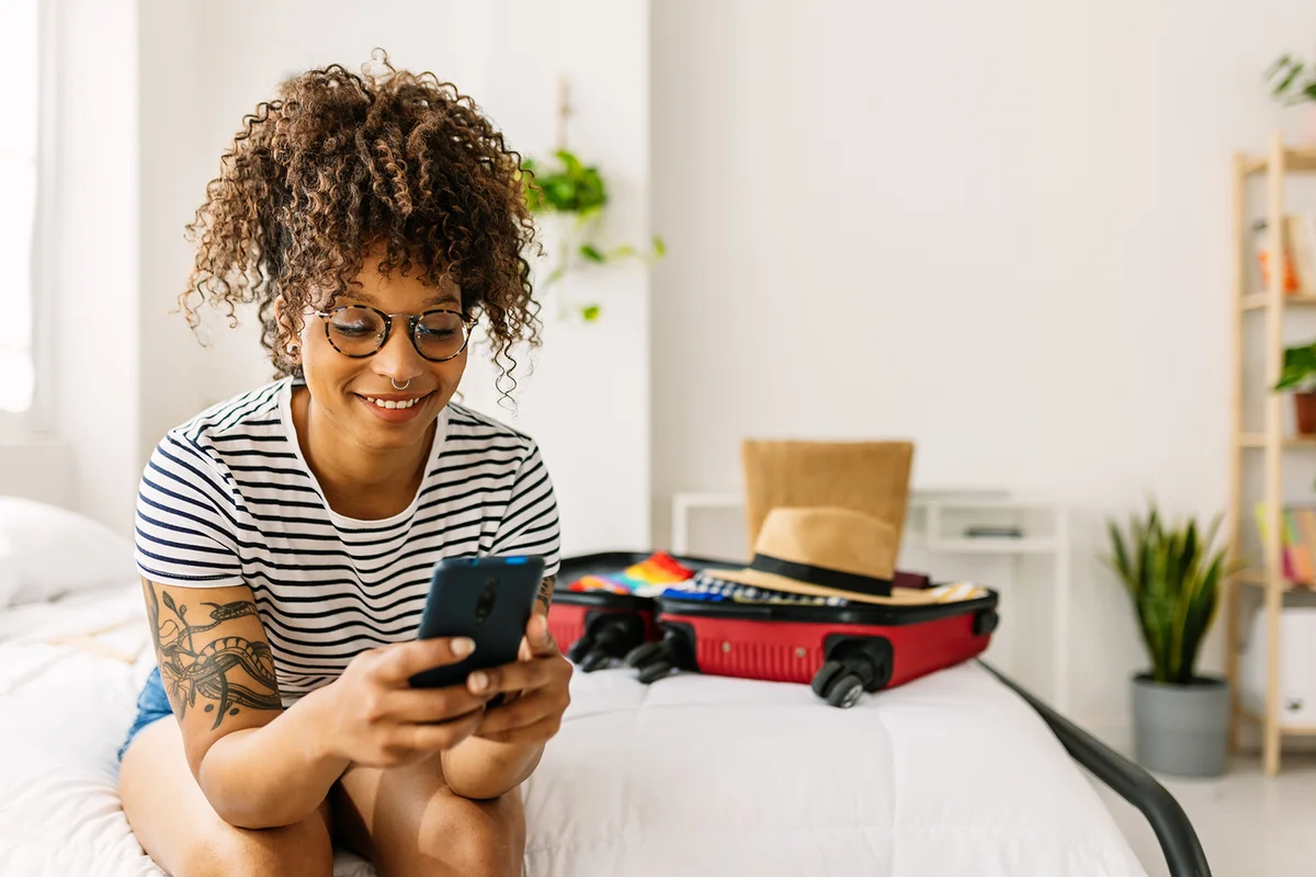 woman booking a hotel room while packing her summer suitcase for holidays