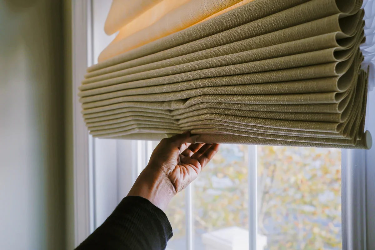 Woman Adjusts Roman Shade on Window