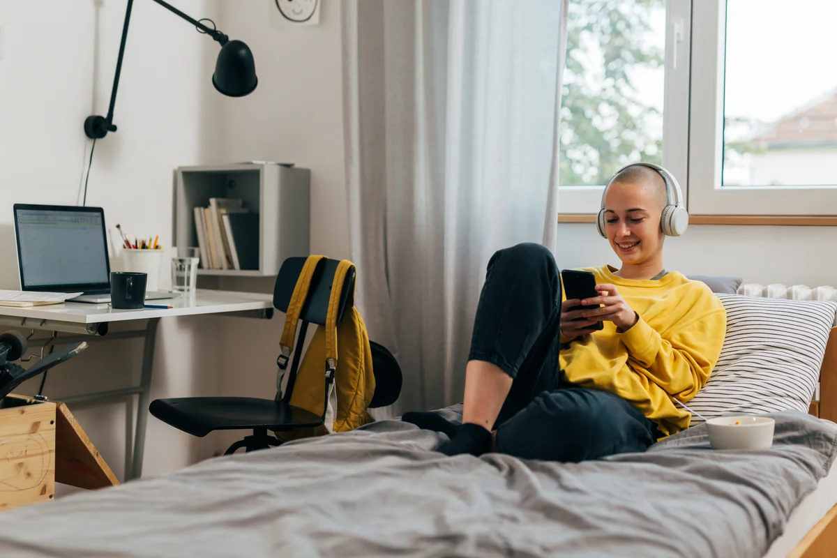 student with phone and laptop in dorm