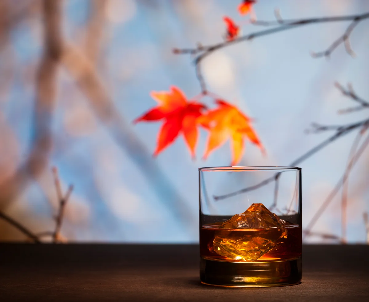A glass of bourbon in front of fall maple leaves