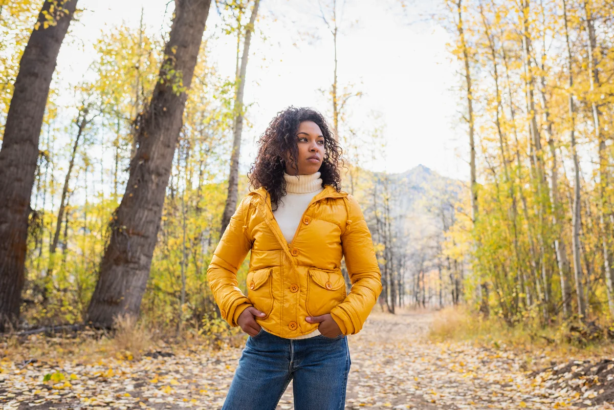 Woman wearing yellow fall coat in the autumn woods